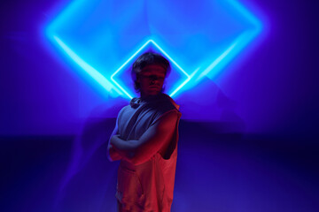 Futuristic portrait of handsome, calm man posing in neon light against background illuminated...