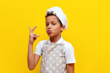 african american boy in chef's uniform and hat shows an italian gesture on yellow isolated...