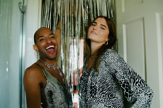 Young non-binary person of Caribbean mixed race and young white woman posing with silver tinsel and smiling