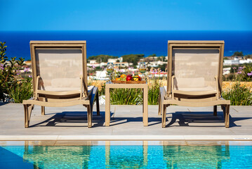 Sunny summer day by the pool, two sunbeds overlooking panoramic sea view. 