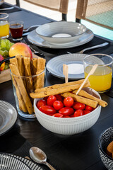 Close-Up Meal Concept: Table Set for Dining with Cherry Tomatoes, Dried Breadsticks, and Orange Juice. Ideal for use in food blogs, lifestyle publications, and promotional materials.