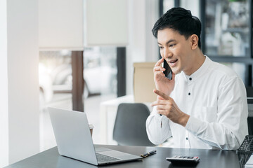 Smiling Asian young freelancer working from home remotely.He is talking on the phone.
