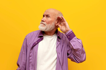 old bald grandfather in purple shirt eavesdropping on secret on yellow isolated background, elderly...