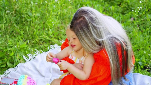 A mother hugs her daughter while sitting in a field of flowers. Concept of happy childhood and parental love for children, warmth and smiles. High quality 4k footage