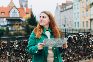Young pretty 30s woman with backpack holding paper map against the Millers Guild house and the...