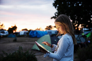 Girl using tablet PC while camping at sunset