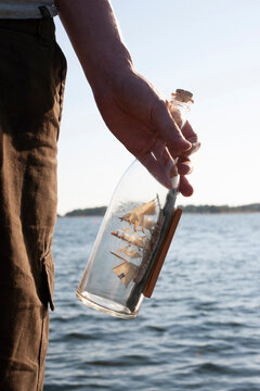 Hand of man holding ship in bottle by sea