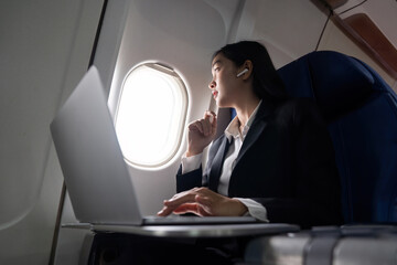 Beautiful businesswoman asian sitting near window on airplane listen music in earphones while...