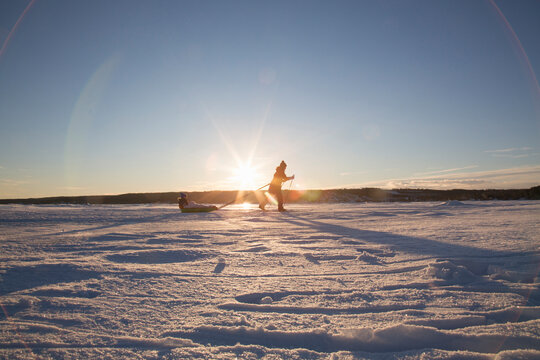 Woman pulling her son in toboggan at sunset