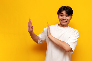 young asian guy in white t-shirt refuses and avoids on yellow isolated background, korean man...
