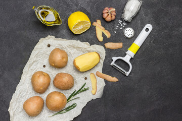 Raw potatoes and one peeled potato on white paper with rosemary, green pepper and lemon © 201122