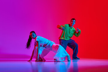 Obraz premium Creative flow. Young man and woman in motion, dancing hip hop against pink red background in neon light. Concept of hobby, action, street style, contemporary dance, youth, fashion