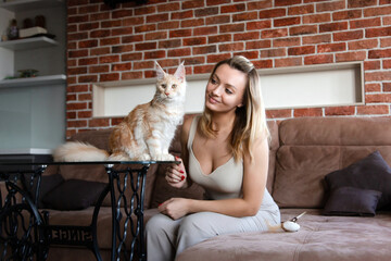 Young smiling woman with ginger and white maine coon cat at home.