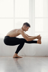 Fototapeta na wymiar Muscular flexible athletic man doing yoga asana at home near big window, Healthy young man engages in home yoga stretch pose.