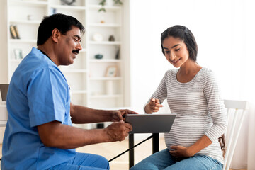 Obraz premium Smiling doctor showing digital tablet with test results to pregnant indian woman