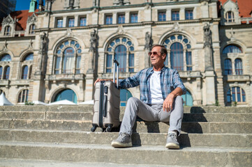 Man traveler with suitcase sitting on stairs on city street.