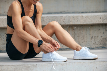 Female kneeling and tying shoelace on street on sunny day.