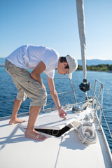 Young guy in white shirt and cap on the yacht fixing a rope