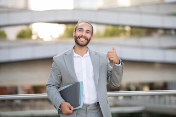 Happy Young Businessman Posing Outdoors, Holding Laptop And Showing Thumb Up