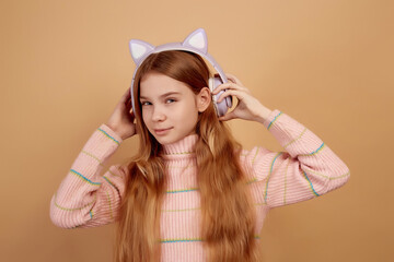 Tricky little girl in headphones with ears eavesdrop on beige background