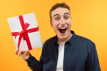 Happy young guy holding wrapped box, feeling excited on yellow