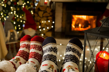 Couple enjoying by warm fireplace and warming up their feet in woolen socks with Christmas...