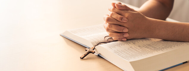Asian male folded hand prayed on holy bible book while holding up a pendant crucifix. Spiritual,...