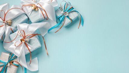 Gift boxes wrapped in blue, white and silver paper with white, blue and gold ribbon bows. Blue background, top view. Christmas and New Year gifts, Boxing Day.