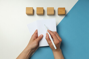 Wooden cubes and hands with paper and pen on white and blue background, top view