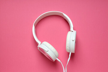 White, on-ear headphones with a wire on a pink background.