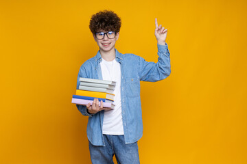 Curly teenager schoolboy with books, on a yellow background.