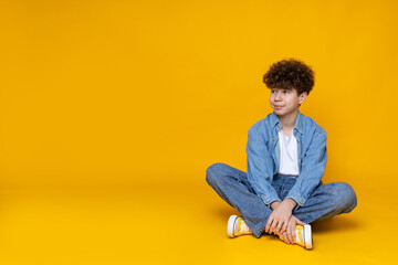 Curly boy teenager sitting on the floor, on a yellow background.