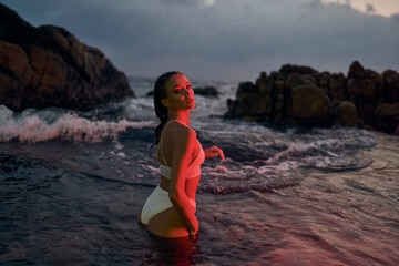 Attractive female enjoys serene night dip in ocean, red illumination enhancing beauty, travel in...