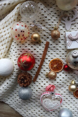 Various colorful Christmas ornaments, small presents and seasonal spices on white knitted blanket. Top view.