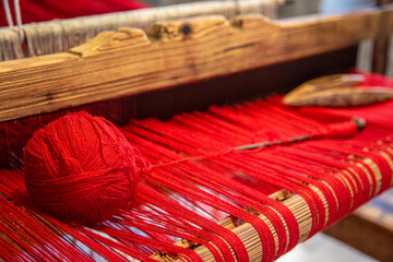 Detail of a ancient loom with a ball of red yarn.