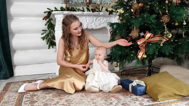 A beautiful mother with a little daughter in her arms decorates the Christmas tree in the living room. New Year's gifts under the tree. large bright room prepared for Christmas. sweet family. High qua