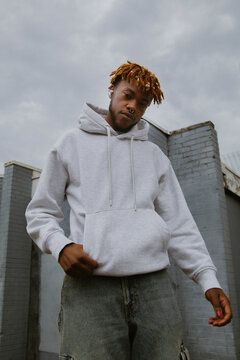 Young black man in street style outfit and ear pods posing in urban area
