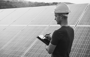 Engineer working at solar panels factory outdoor - Photovoltaic, renewable green energy and environmental concept - Focus on face - Black and white editing