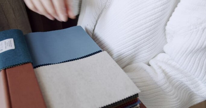 Closeup of female hands hold catalog with fabric swatches and choosing colour for decoration interior. Cropped view on woman designer select textile for curtains or furniture. Improvement indoors