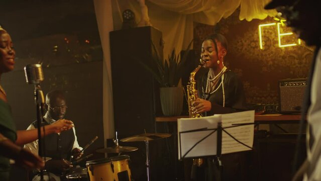 Medium shot of Black jazz band of four giving live concert on stage with warm dimmed light at fancy jazz club