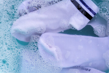 Dirty white socks soaked in water, dissolving detergent in blue basin.