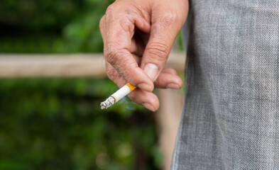 Close up male hand holding a cigarette at outdoor on nature background.