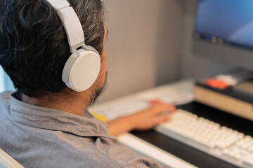 View from the shoulder of businessman in shirt working inside office using computer with headphones