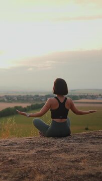 Back view of calm brunette woman meditating and sitting at lotus pose at the nature