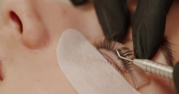 Closeup on woman client on lash lamination procedure in beauty salon. Beautician in gloves doing professional eyelash care treatment to female.