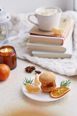 Aesthetics dessert bright orange macaroon, tangerines among books, candle and coffee. Festive table setting