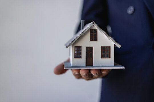 Real estate agent holds a model of a house offered to his client after signing the sales contract at the office. Real estate investment concept and businessman's hands holding wooden model