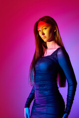 Portrait of beautiful young woman in elegant dress posing against gradient pink background with...