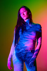 Portrait of young beautiful girl posing against gradient pink green background with neon...