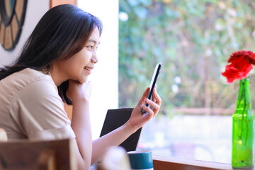 happy asian woman sit in cafe using smartphone with laptop on table wearing fashionable clothes,...